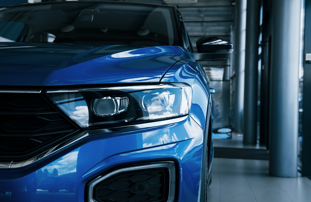 Close-up of the front left headlight and grille of a blue car parked indoors, its surface gleaming with reflections—a testament to expert Auto Paint Correction in New Orleans.