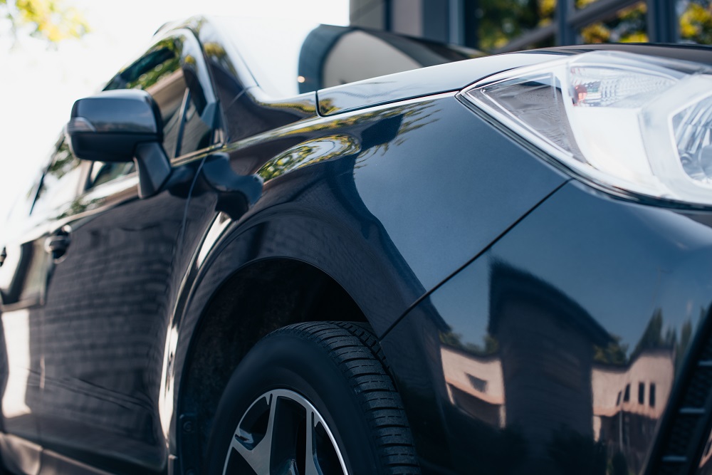 Close-up view of the front left side of a dark-colored car parked outdoors, showing the headlight, wheel, and glossy reflections—highlighting results from Mobile Auto Detailing in Mandeville, LA.