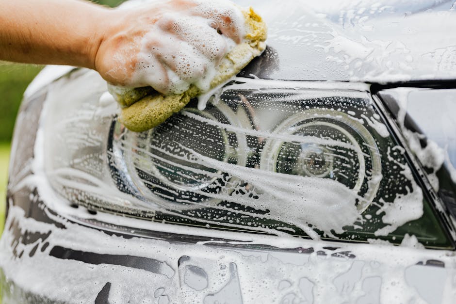 Hand cleaning a car headlight with a sponge and soap as part of regular maintenance after headlight restoration