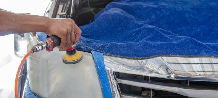 Professional technician polishing a car headlight with an electric buffing tool during headlight restoration service in New Orleans