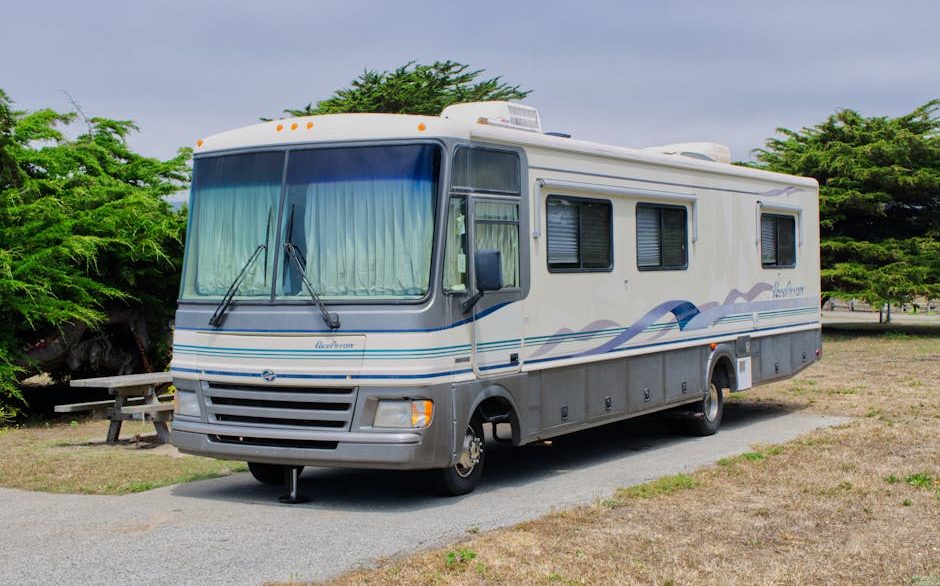 Detailer cleaning the fiberglass exterior of a large RV in a New Orleans driveway