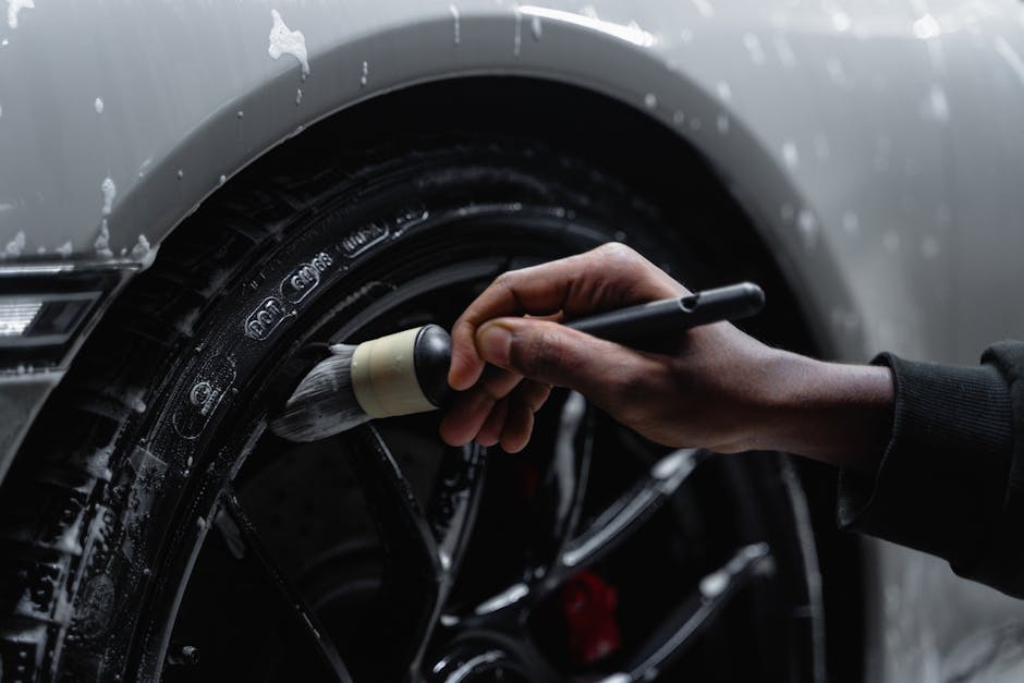 Professional detailer cleaning brake dust from a car wheel with a specialized brush in New Orleans